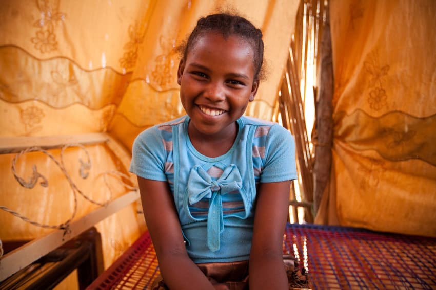  A lively young girl sitting on her bed in her tent