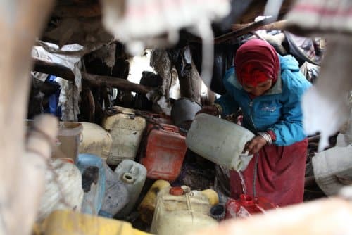 A woman in Tunisia carefully pours water into drums for storage.