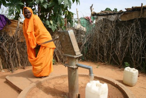 A Sudanese woman fills up a drum with water.